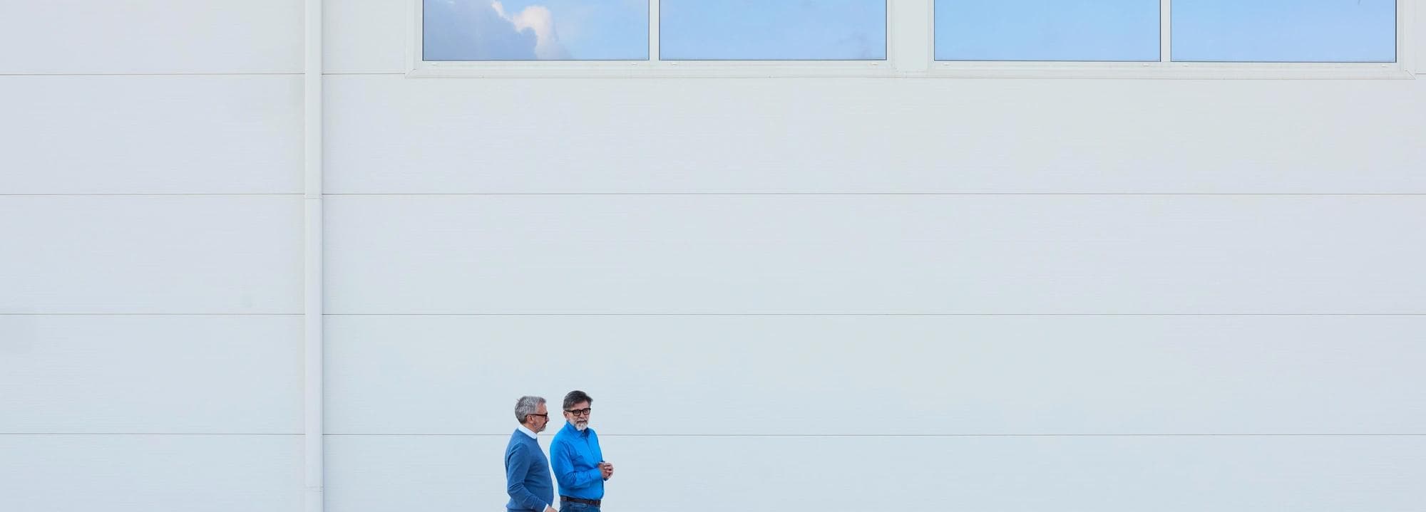 Deux personnes marchent près d'un bâtiment moderne blanc avec des lignes architecturales claires.